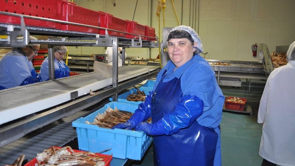Woman wearing hairnet and rubber gloves and apron in a fish facility