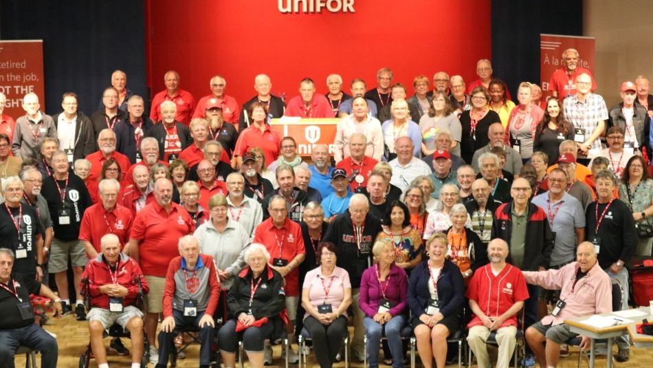 A group of people with a red Unifor stage in the background.