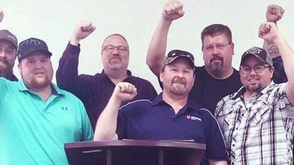 Members of Local 112, standing behind a podium, raise thier fists in solidarity.